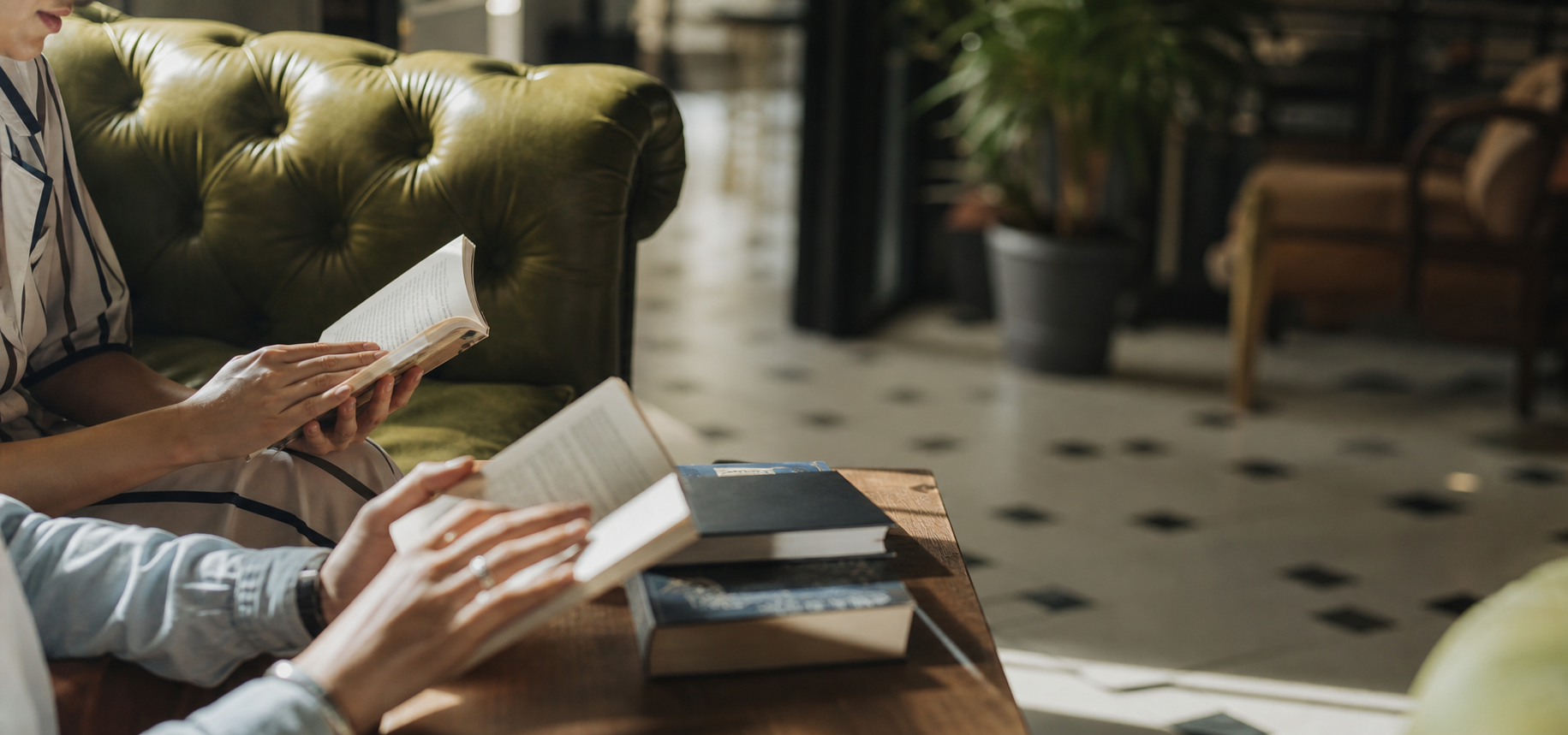 Two people read books at a table in a relaxed cafe-style reading space.